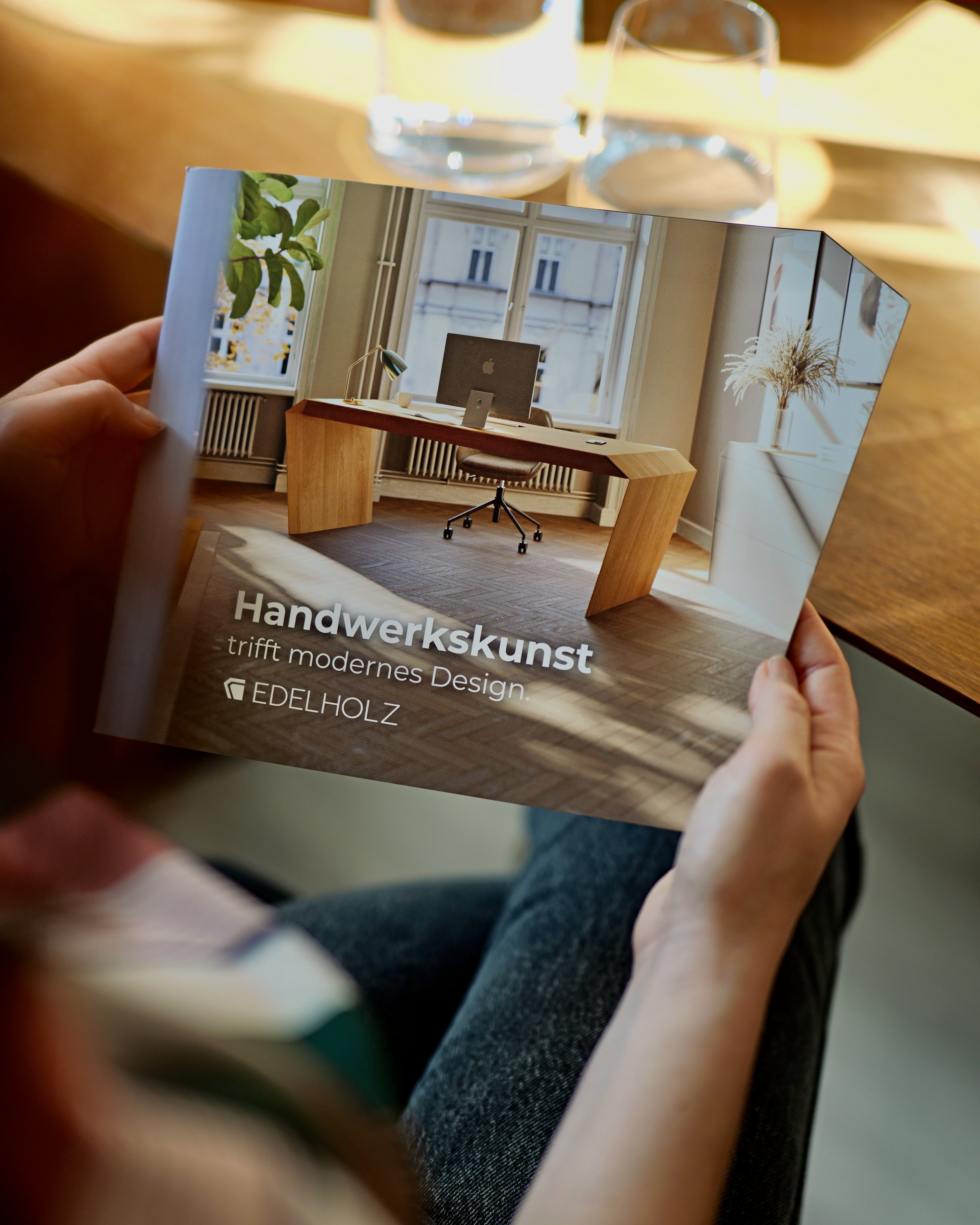 EDELHOLZ Broschüre mit Cover Handwerkskunst trifft modernes Design in den Händen einer Person über Holztisch