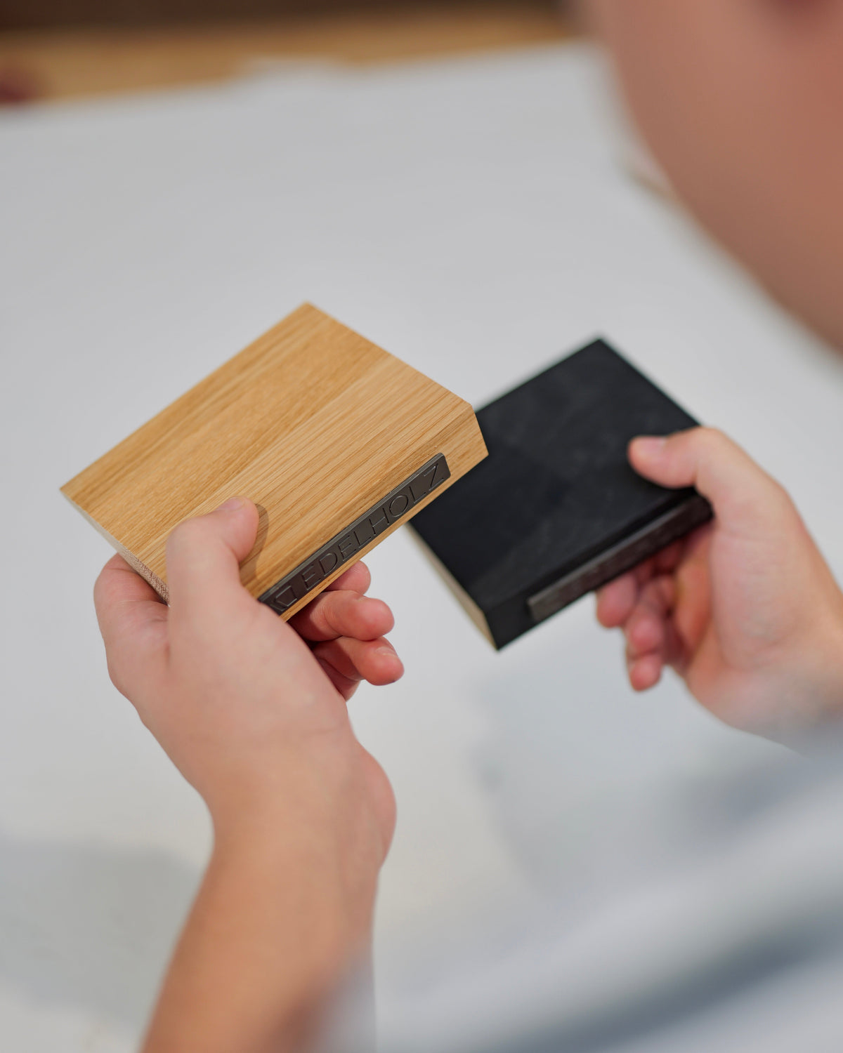 Hände halten zwei EDELHOLZ Holzmuster aus Eiche und Midnight Noir mit eingelaserter Markenprägung im Vergleich
