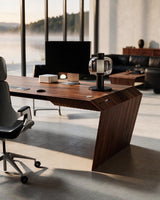 EDELHOLZ DeskPRO Schreibtisch in Deep Walnut, Raumansicht mit Bürostuhl, Monitor und Tischleuchte vor bodentiefen Fenstern [finish:deep-walnut]
