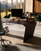 EDELHOLZ DeskPURE Schreibtisch in Smoked Amber, Raumansicht mit Bürostuhl, Monitor und Tischleuchte vor bodentiefen Fenstern [finish:smoked-amber]